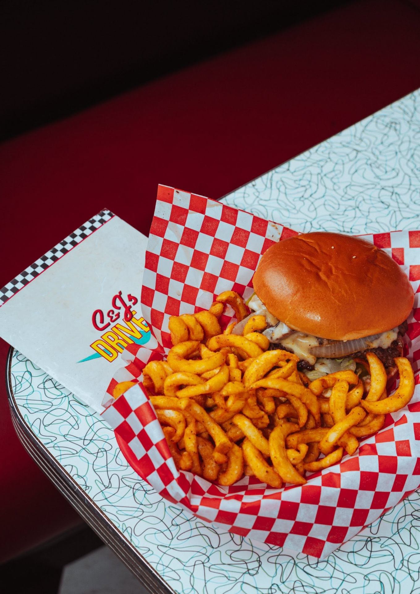 Smash burger with curly fries in a red checker basket