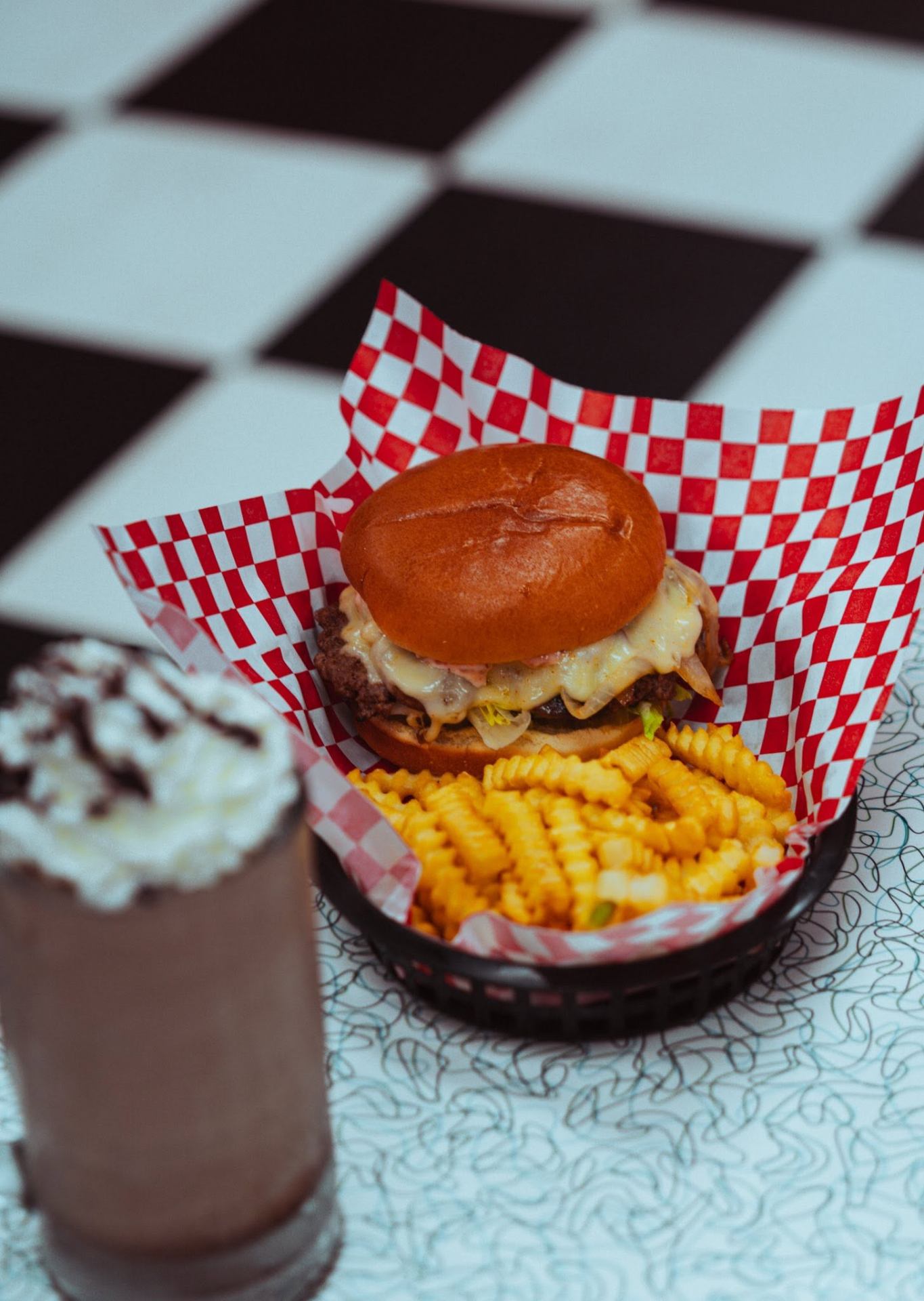 Cheeseburger with crinkle fries and a chocolate shake on a checker floor